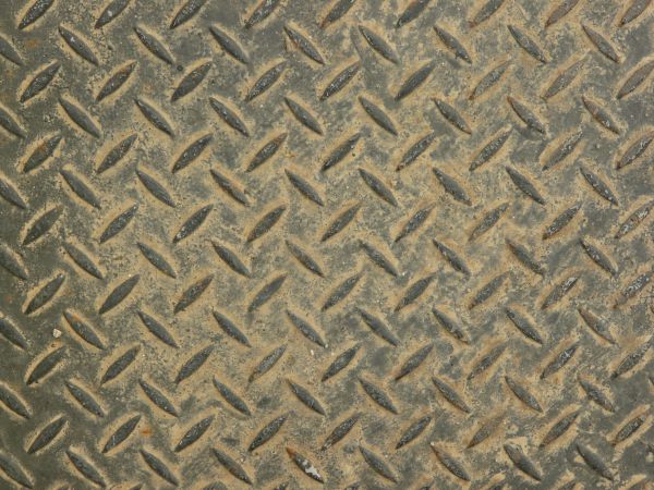 Metal tread texture in dark brown tones with leaf-like pattern on worn surface.